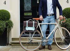 Don Dark Brown and Cambridge Blue Leather Pannier with male model holding up a bicycle that is holding the pannier
